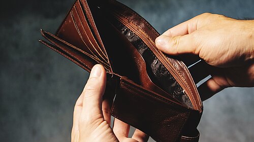 A person opening a wallet to reveal it is empty.