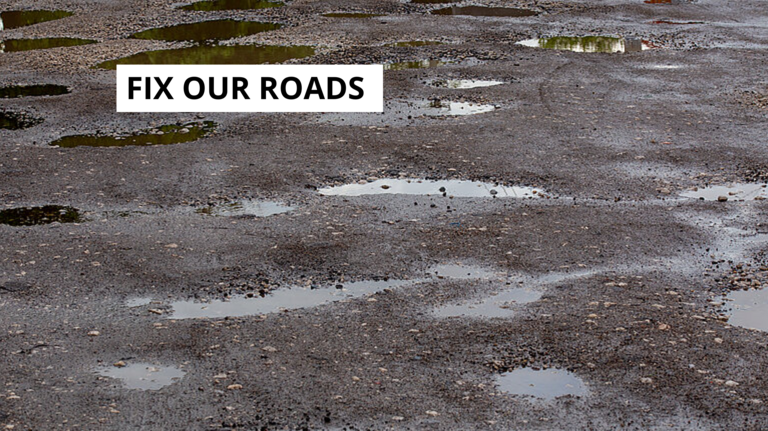 Road with potholes and slogan Fix Our Roads